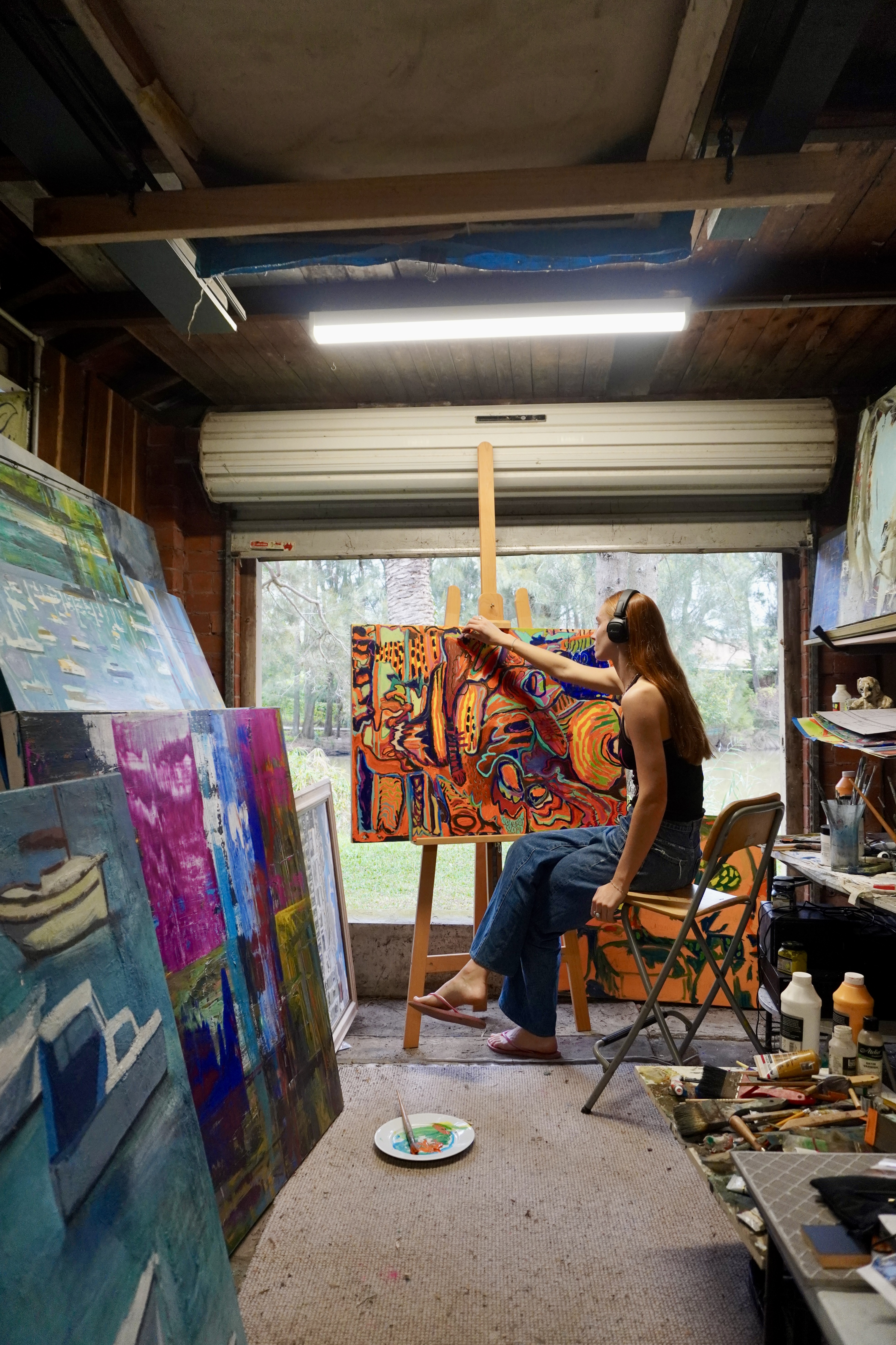Hayley Biddulph painting in her studio, surrounded by vibrant abstract canvases on an easel and leaning against the walls